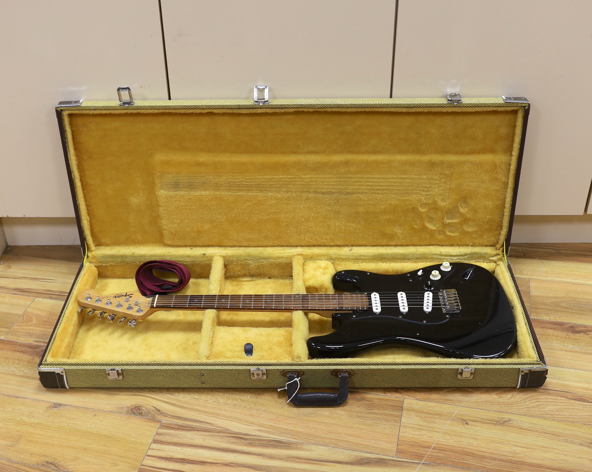 A cased Squier Strat by Fender electric guitar with rosewood neck and balance lacquer body, together with a Harris Tweed flight case